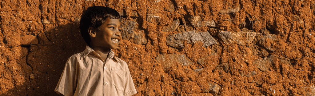 An image of a young boy whose name is apparently Daniel smiling off to his left as he stands near a rust colored stone wall.